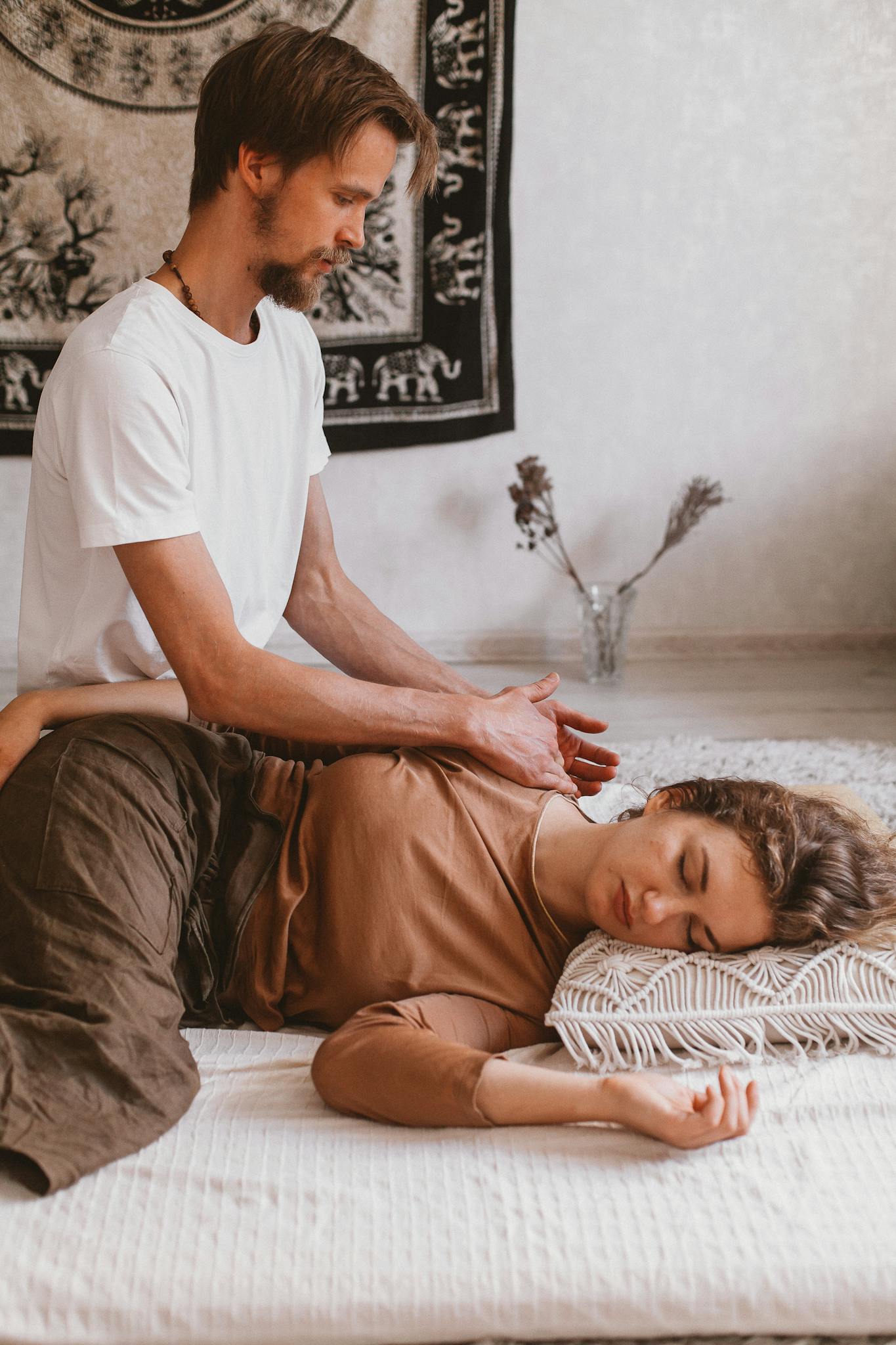 A man giving a relaxing massage to a woman lying on a mat in a peaceful room.